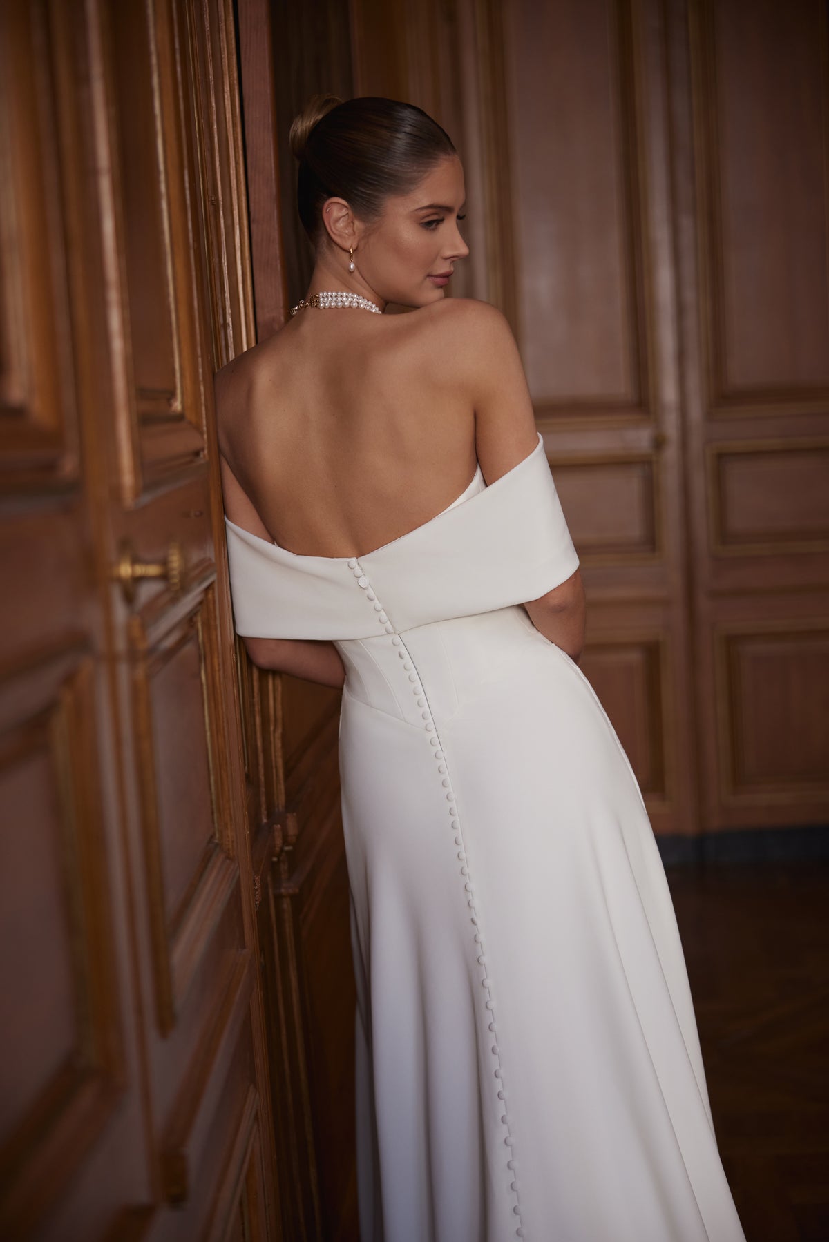 Robe de mariée Calliope, avec un large décolleté aux épaules dénudées et une jupe épurée en satin avec une fente.