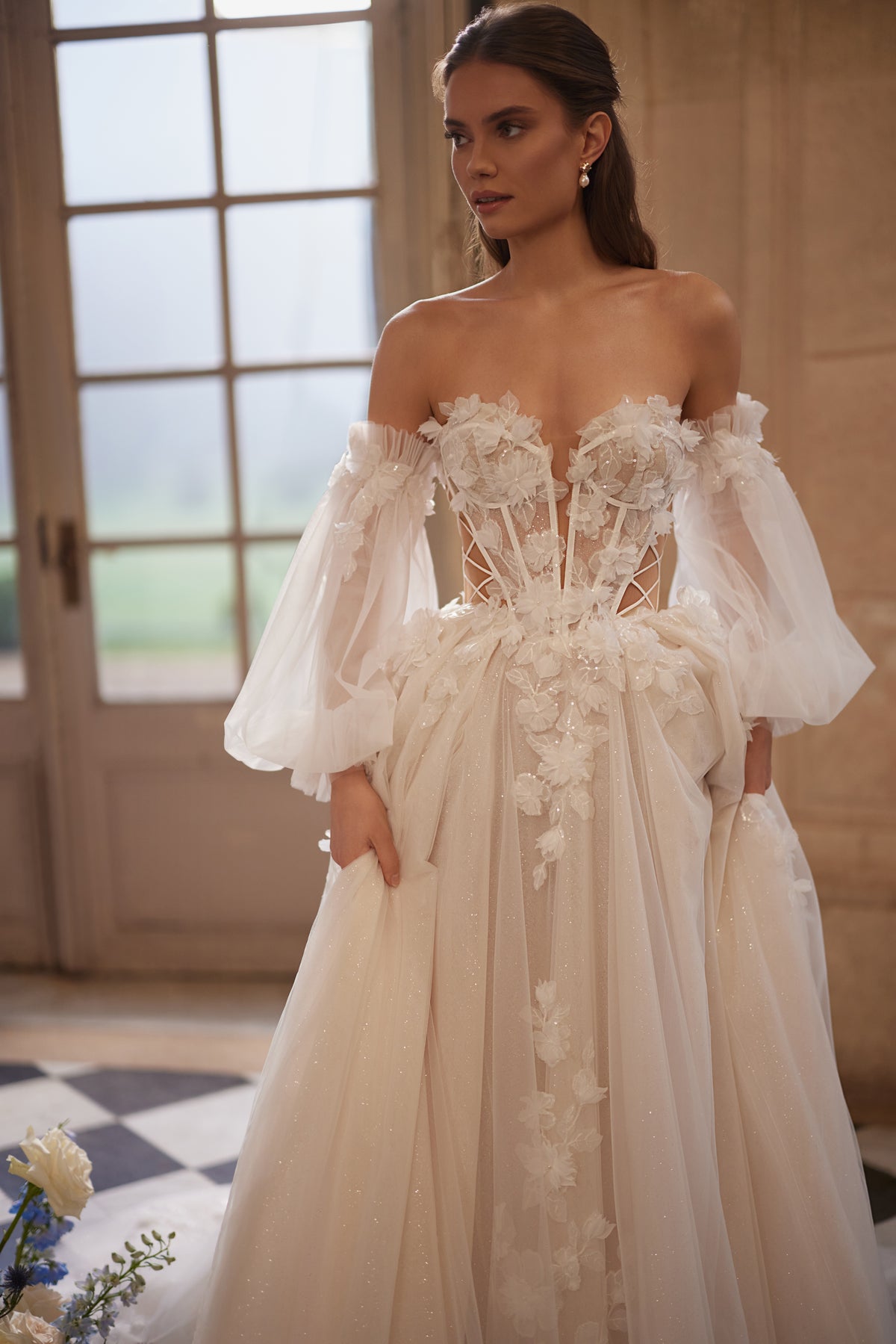 Robe de mariée trapèze Celestine, avec un décolleté ouvert, des manches légères laissant les épaules dénudées et des fleurs en relief.
