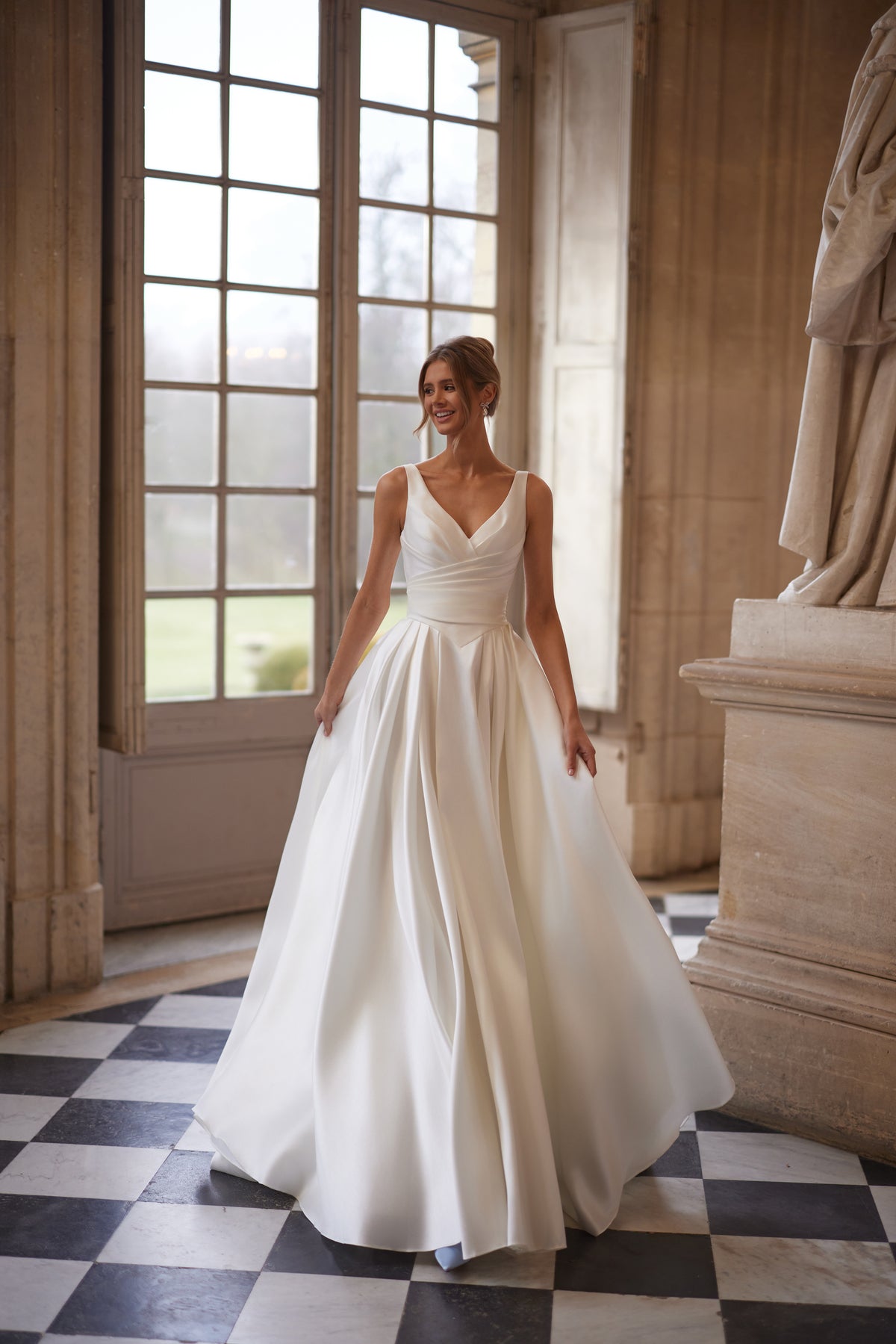 Robe de mariée Elvira, avec un décolleté en V ouvert et une jupe drapée épurée avec une fente haute.