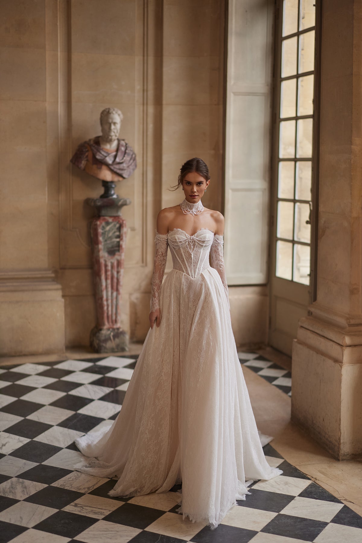Robe de mariée trapèze Blanche, avec un corset perlé, une jupe souple en dentelle et des manches laissant les épaules dénudées.