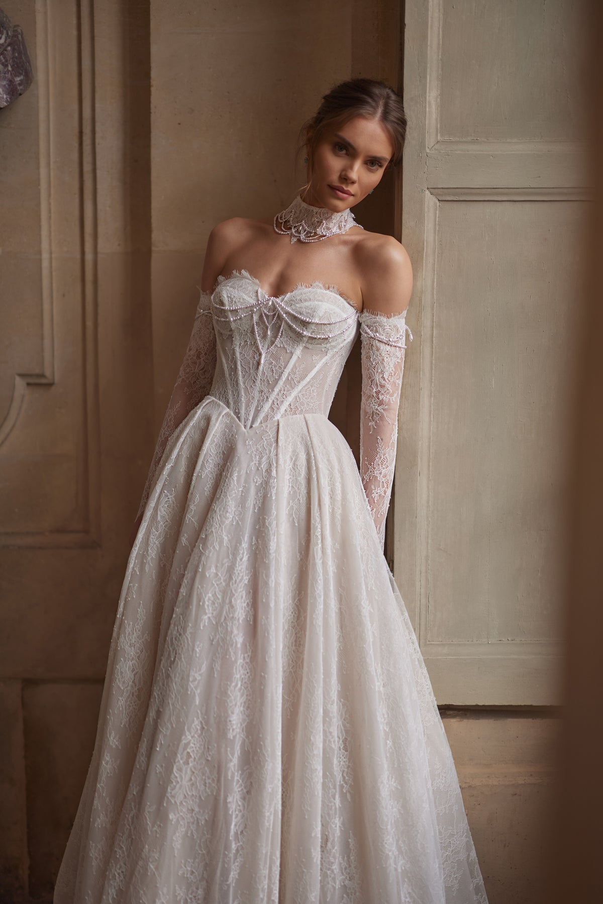 Robe de mariée Blanche, avec un corset perlé, une jupe souple en dentelle et des manches laissant les épaules dénudées — collection Something Blue 2027, DAMA Couture.