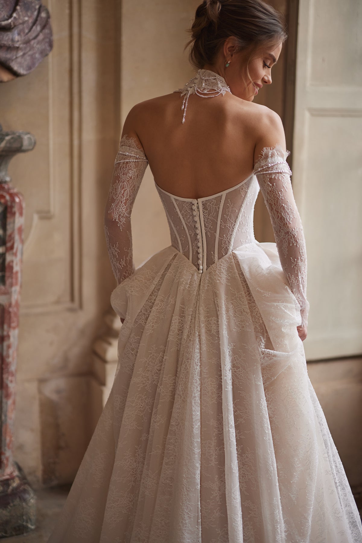 Robe de mariée Blanche, avec un corset perlé, une jupe souple en dentelle et des manches laissant les épaules dénudées.