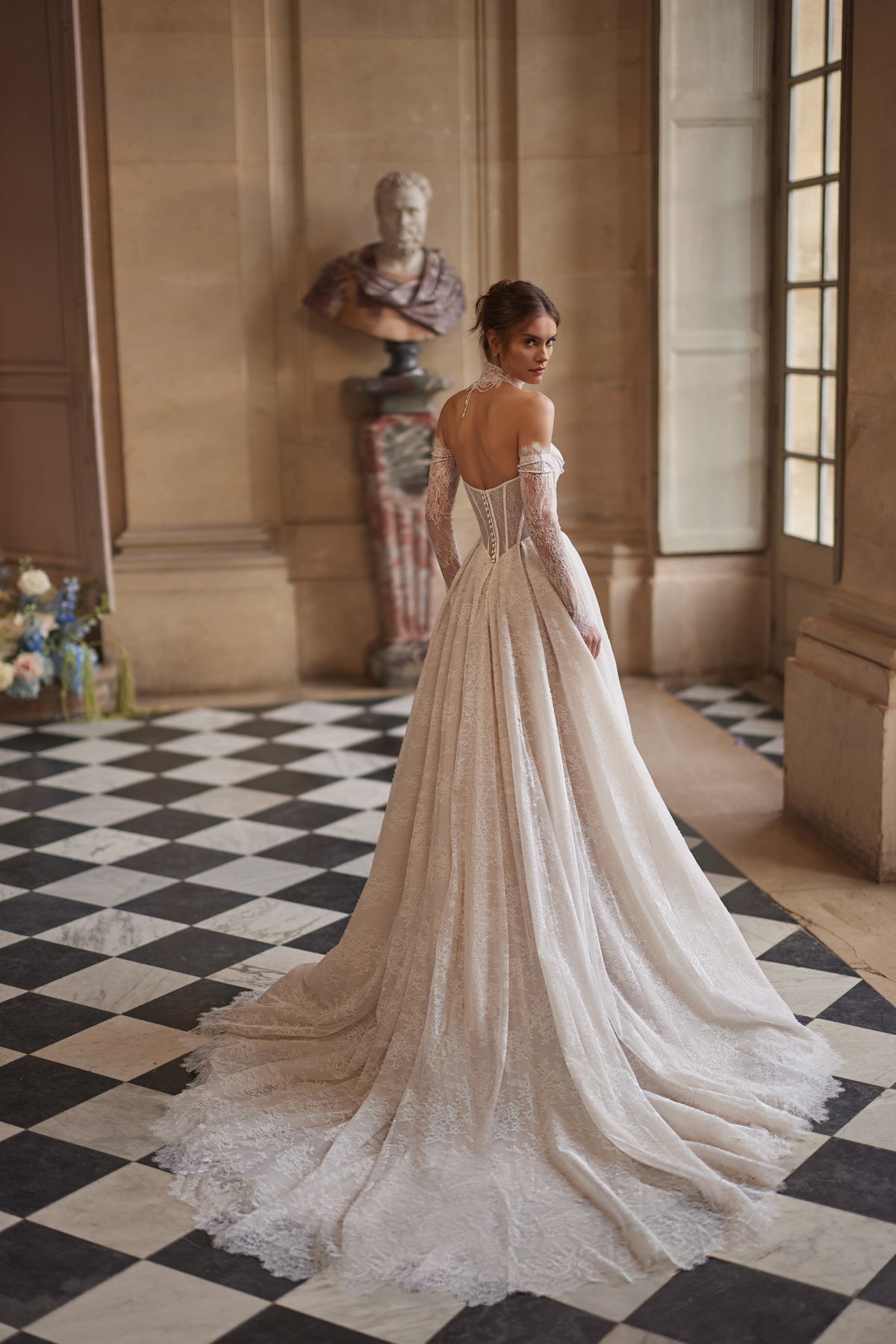 Robe de mariée trapèze Blanche, avec un corset perlé, une jupe souple en dentelle et des manches laissant les épaules dénudées.