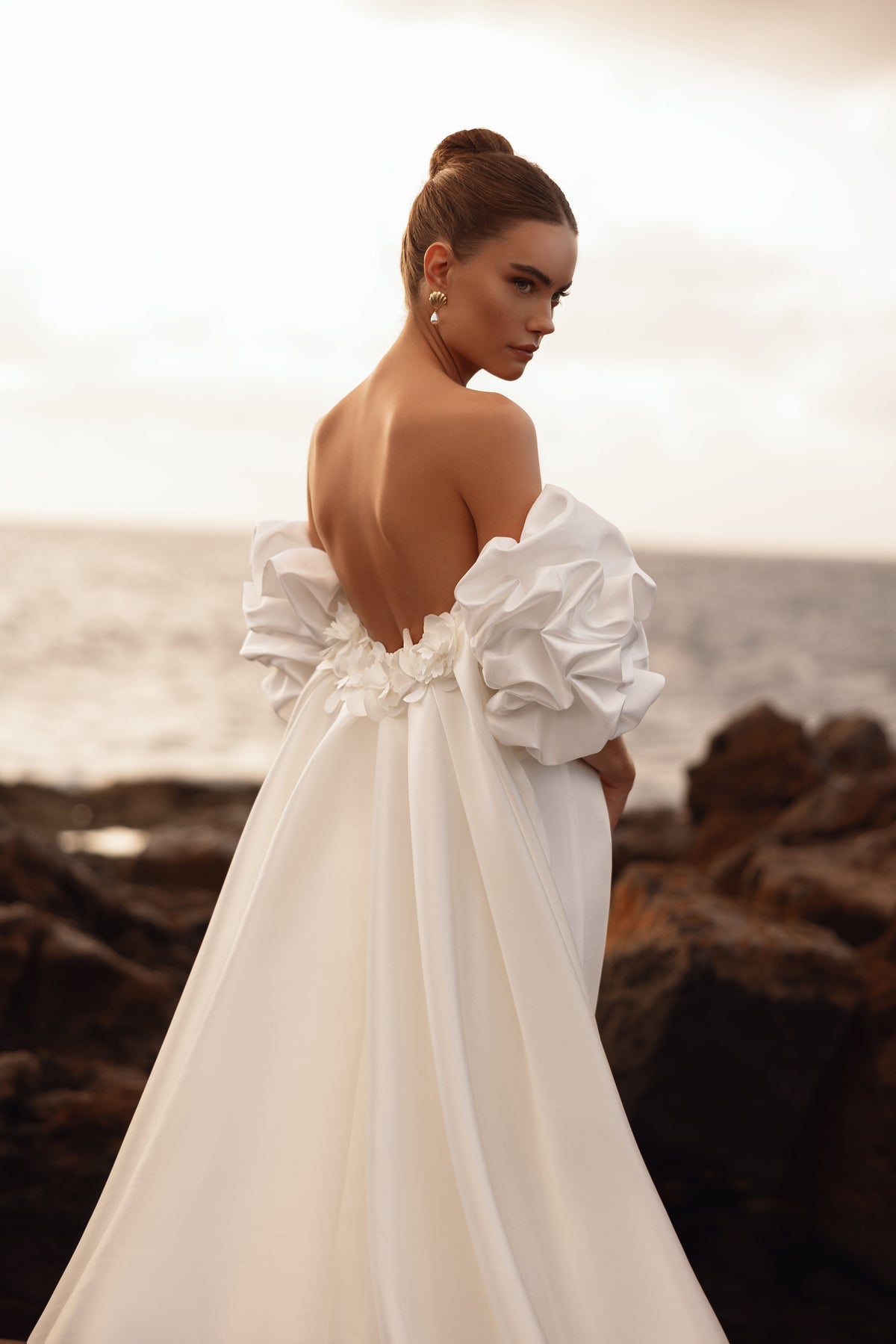 Robe de mariée dos nu, avec des manches bouffantes et de délicats appliqués floraux.