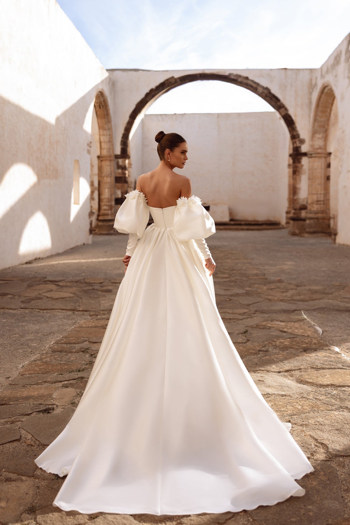 Robe de mariée longue Anika, avec des manches laissant les épaules dénudées et une traîne.