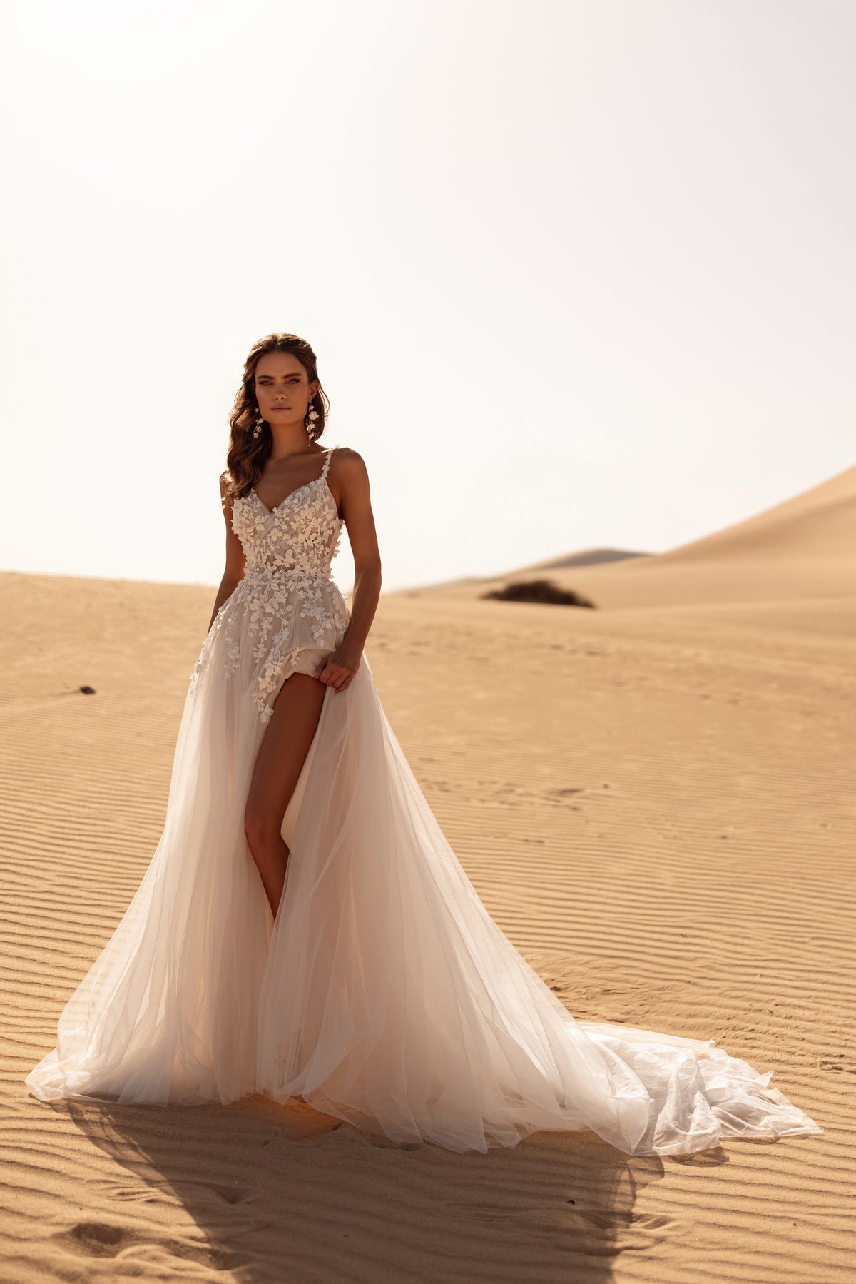 Robe de mariée Aviva, avec une longue traîne et un voile fluide, dans la lumière dorée du désert.