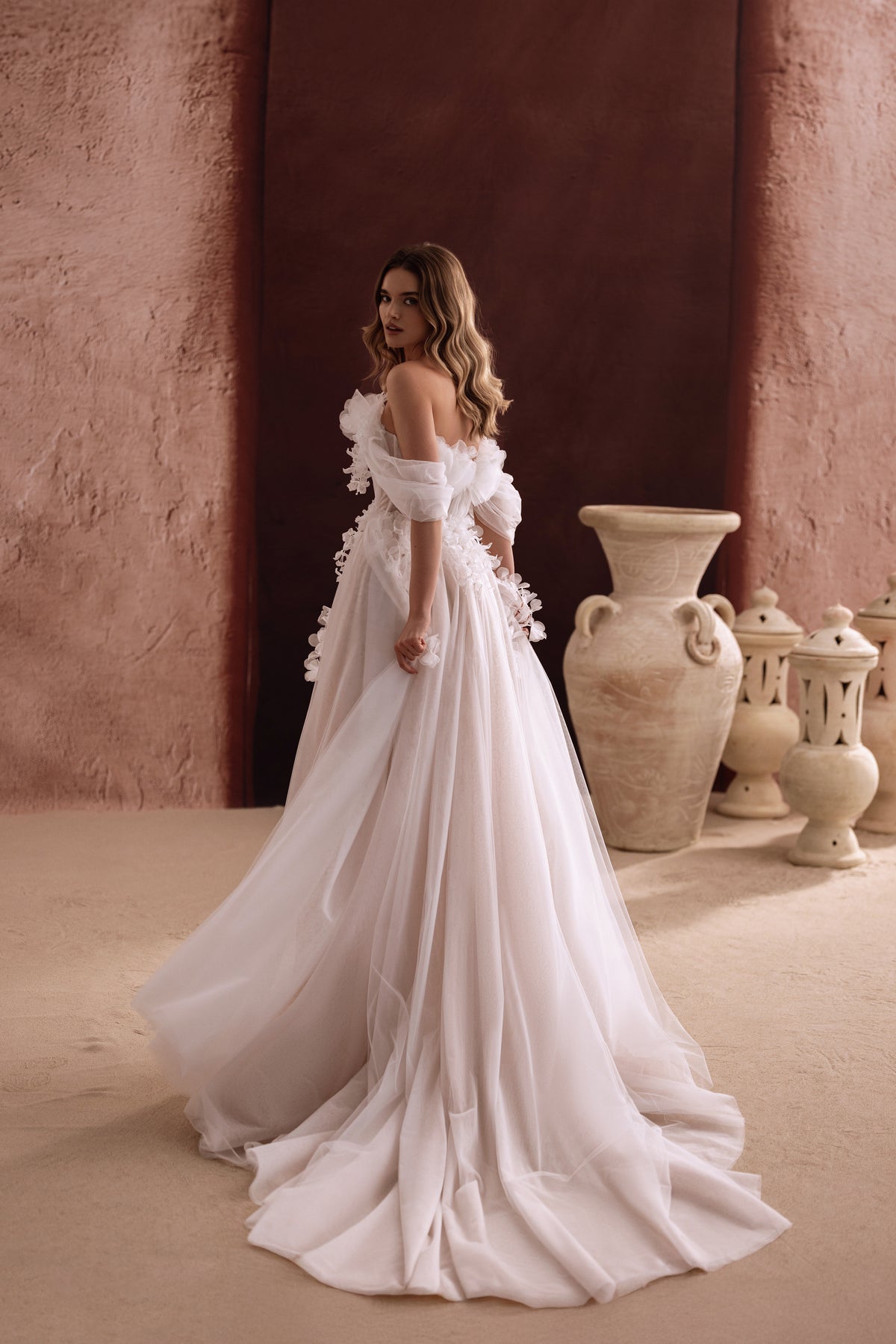 Robe de mariée Bella, avec des manches laissant les épaules dénudées et une traîne fluide en tulle.