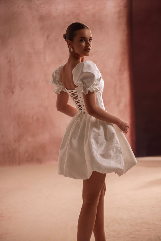 Mini-robe de mariée Daphne, avec un corset lacé dans le dos qui marque la taille et des manches bouffantes.