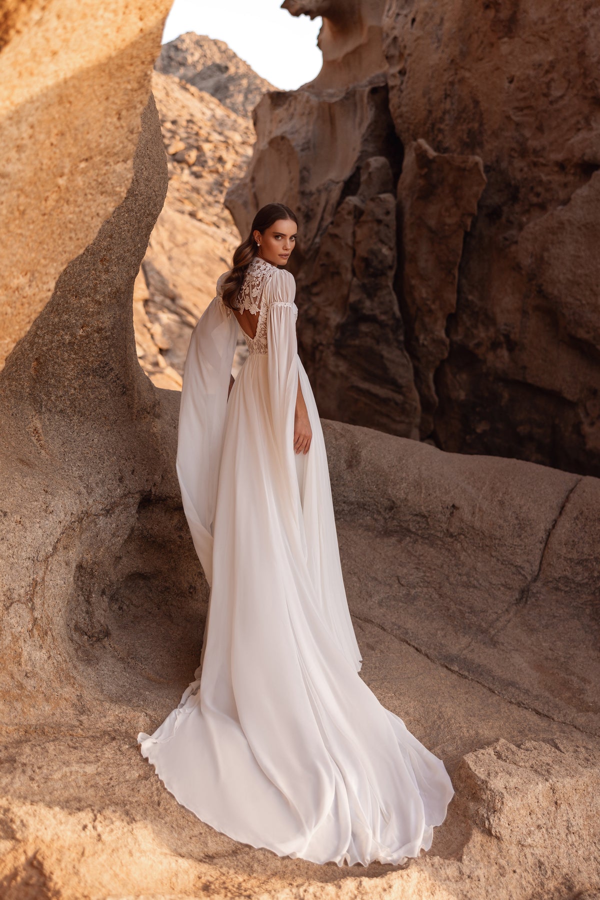 Robe de mariée Etra, avec un décolleté en V profond, une grande fente et des manches cape en mousseline.