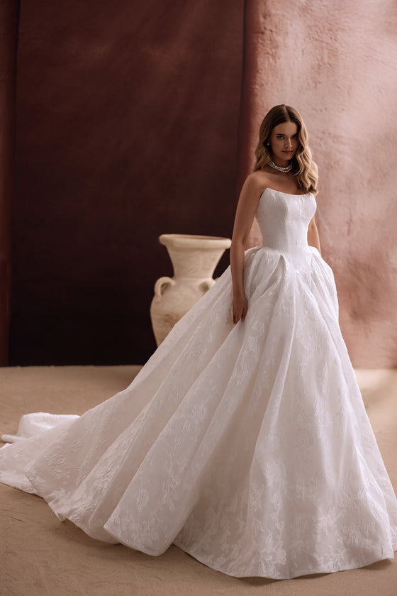 Robe de mariée Hebe, avec une longue traîne cathédrale et un corsage sans bretelles.