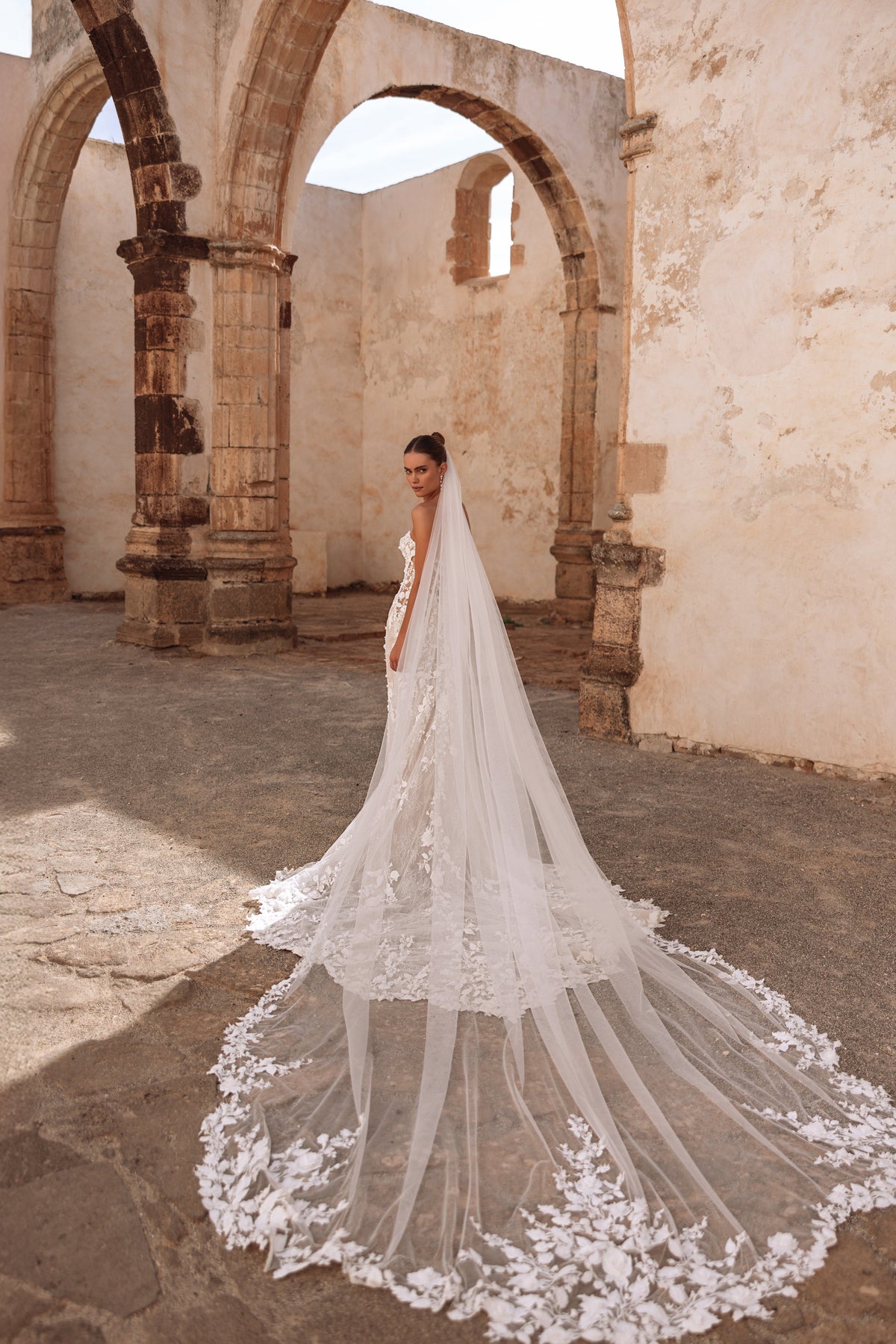 Robe de mariée en dentelle, avec un voile cathédrale et une traîne à appliqués floraux.