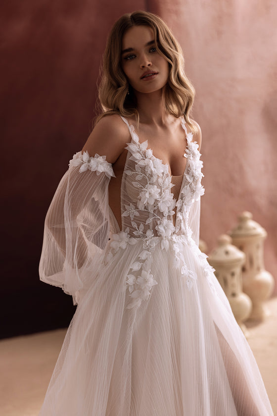 Robe de mariée Lilibeth, avec un décolleté plongeant et des manches bouffantes en tulle nouées par des nœuds.