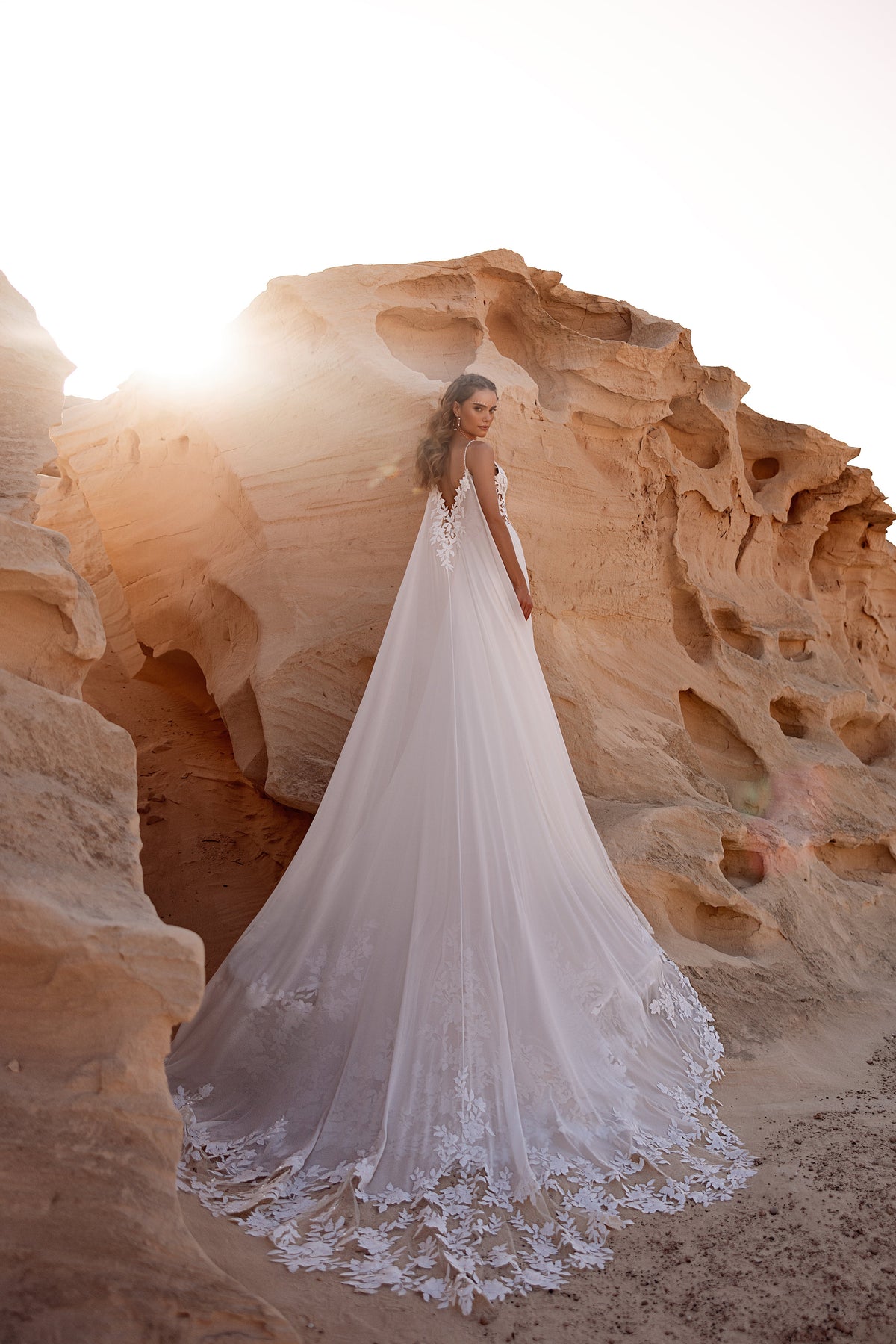 Robe de mariée Malika, avec une longue traîne fluide, dans un paysage désertique.