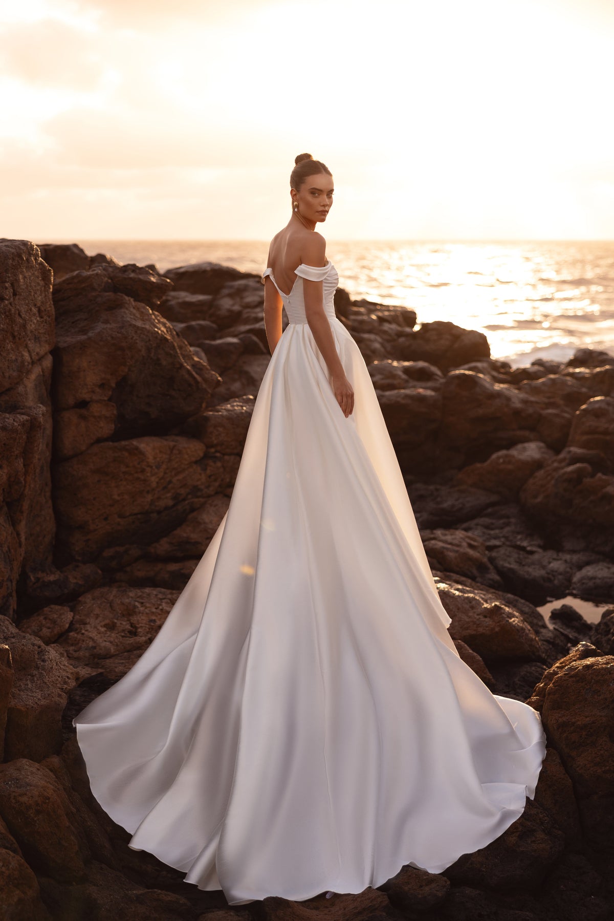Robe de mariée Mellisandre, avec les épaules dénudées et une traîne au coucher du soleil.