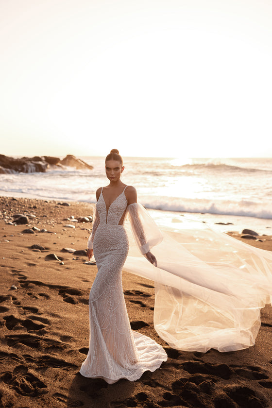 Robe de mariée sirène ajustée, avec un décolleté en V profond et un voile fluide de longueur chapelle, sur la plage.