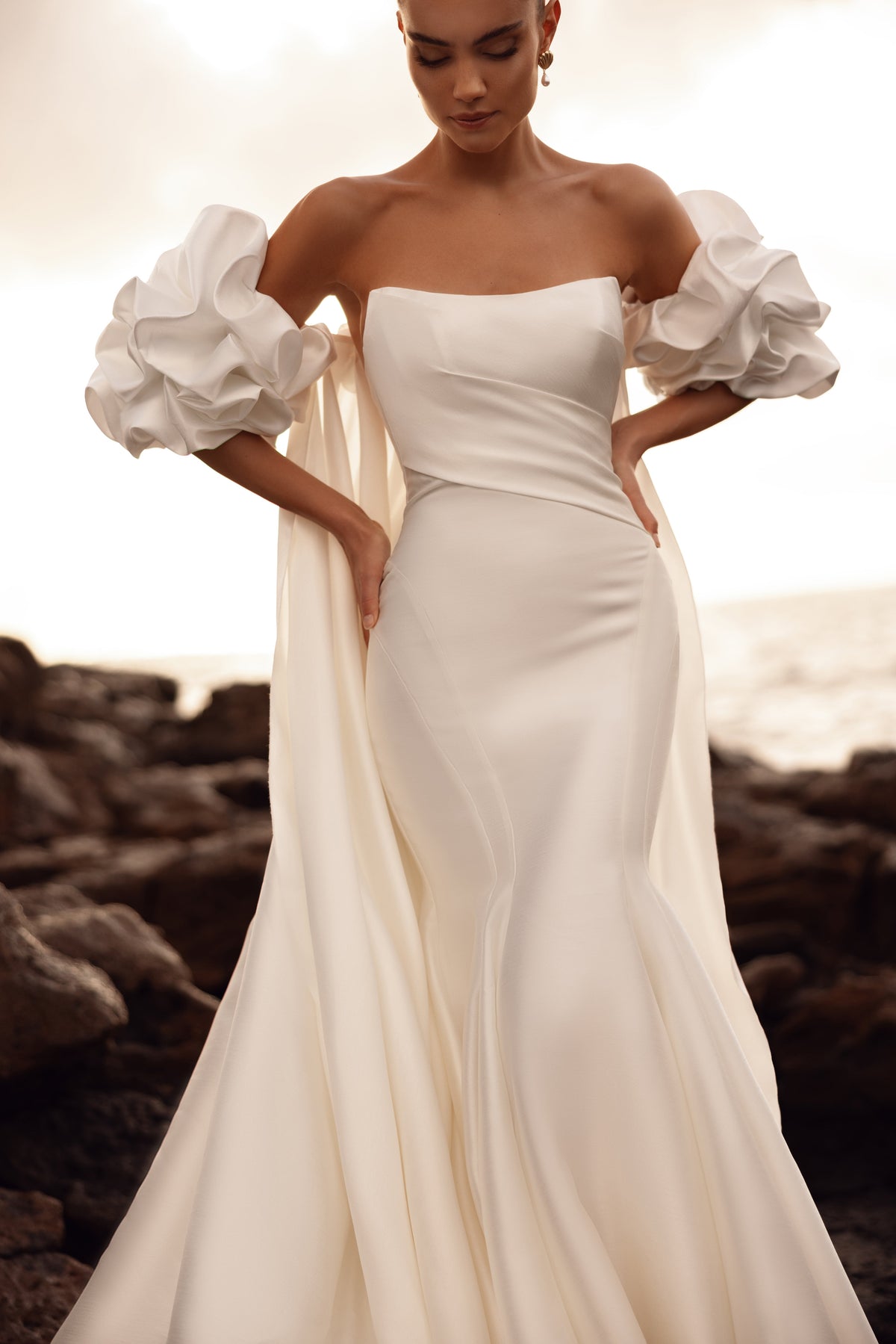 Robe de mariée sirène, avec des manches bouffantes aux épaules dénudées et un corsage structuré qui marque la taille.