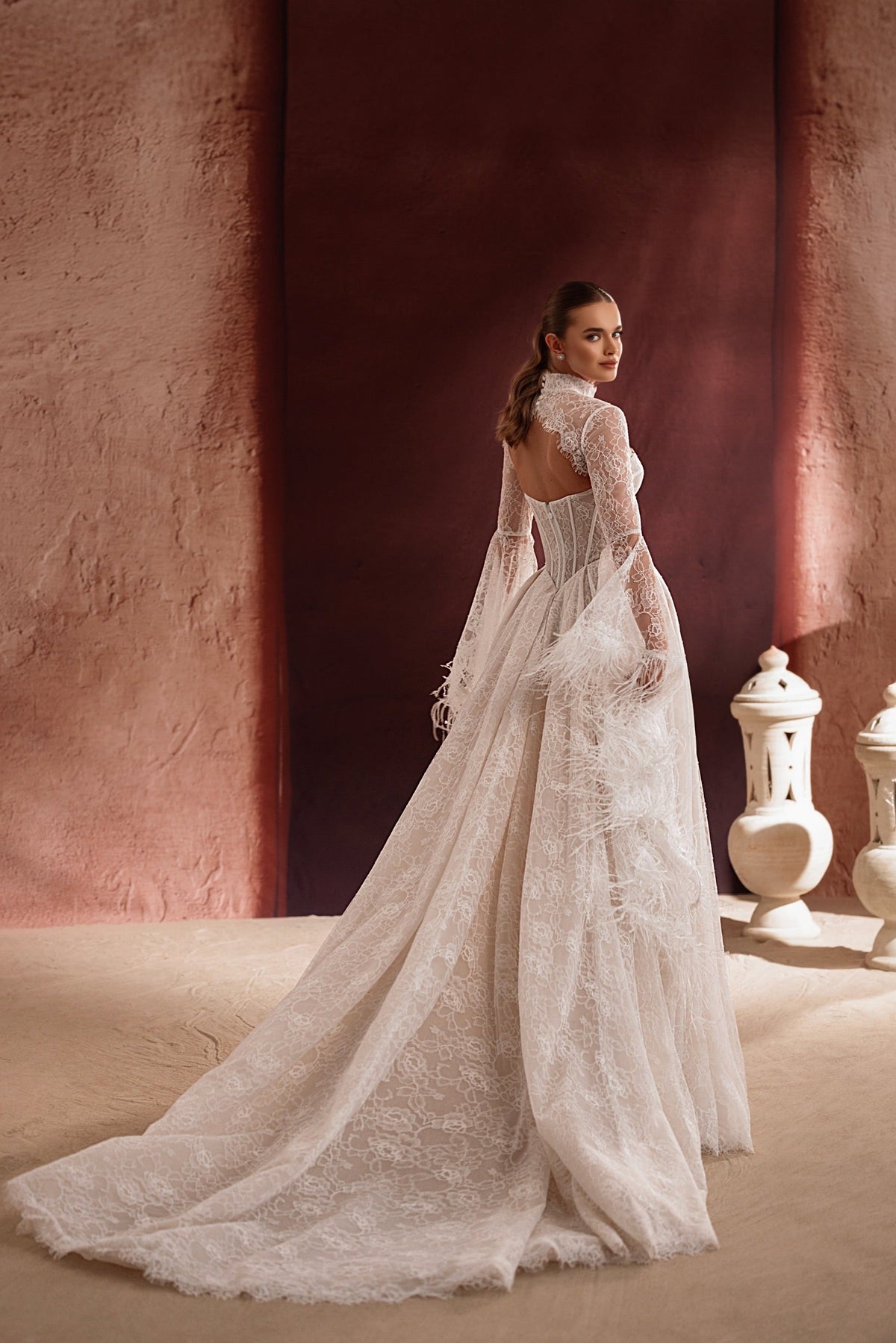 Robe de mariée Michelle, avec un col montant en dentelle, une longue traîne et des détails de plumes.