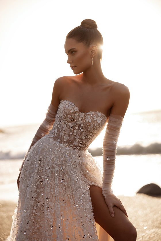 Robe de mariée Reem, avec un corset, une fente haute, des broderies florales en relief et des détails scintillants au coucher du soleil.