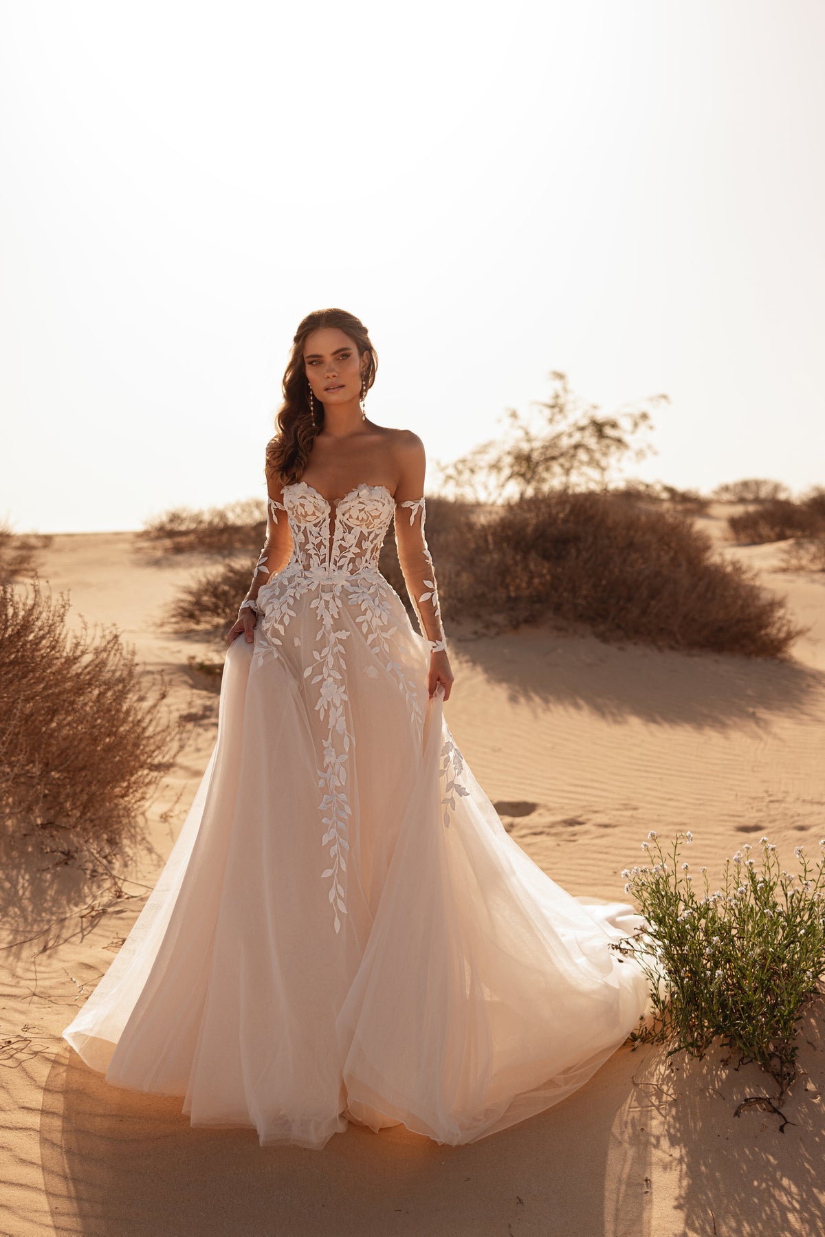 Robe de mariée Tamara, avec un corset aux épaules dénudées et une traîne fluide en tulle, sous le soleil du désert.