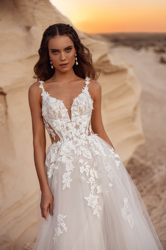 Robe de mariée Zafira, avec une jupe en tulle et des détails de dentelle florale, aux côtés d’un marié en costume beige.