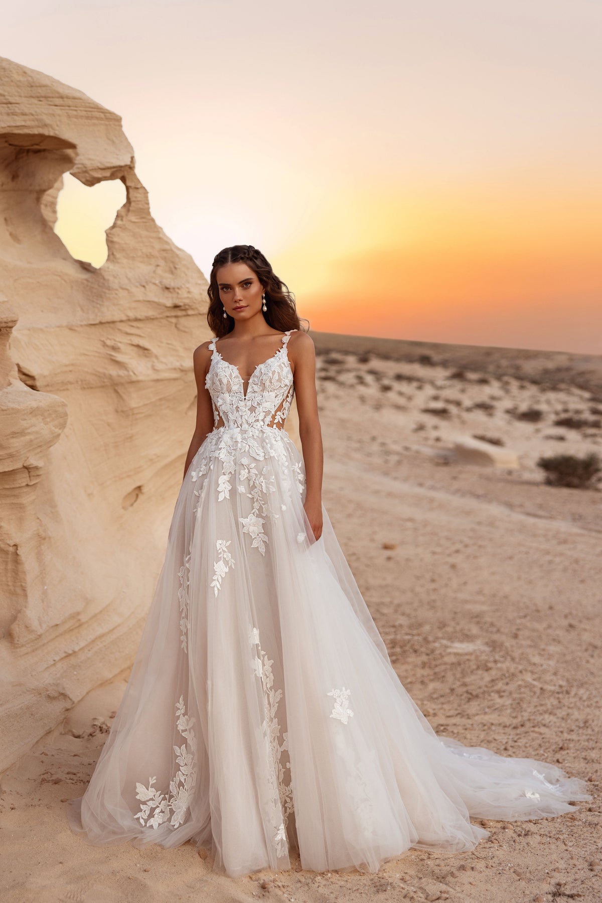 Robe de mariée Zafira, avec un décolleté en V plongeant et des appliqués de dentelle florale en relief, au coucher du soleil dans le désert.